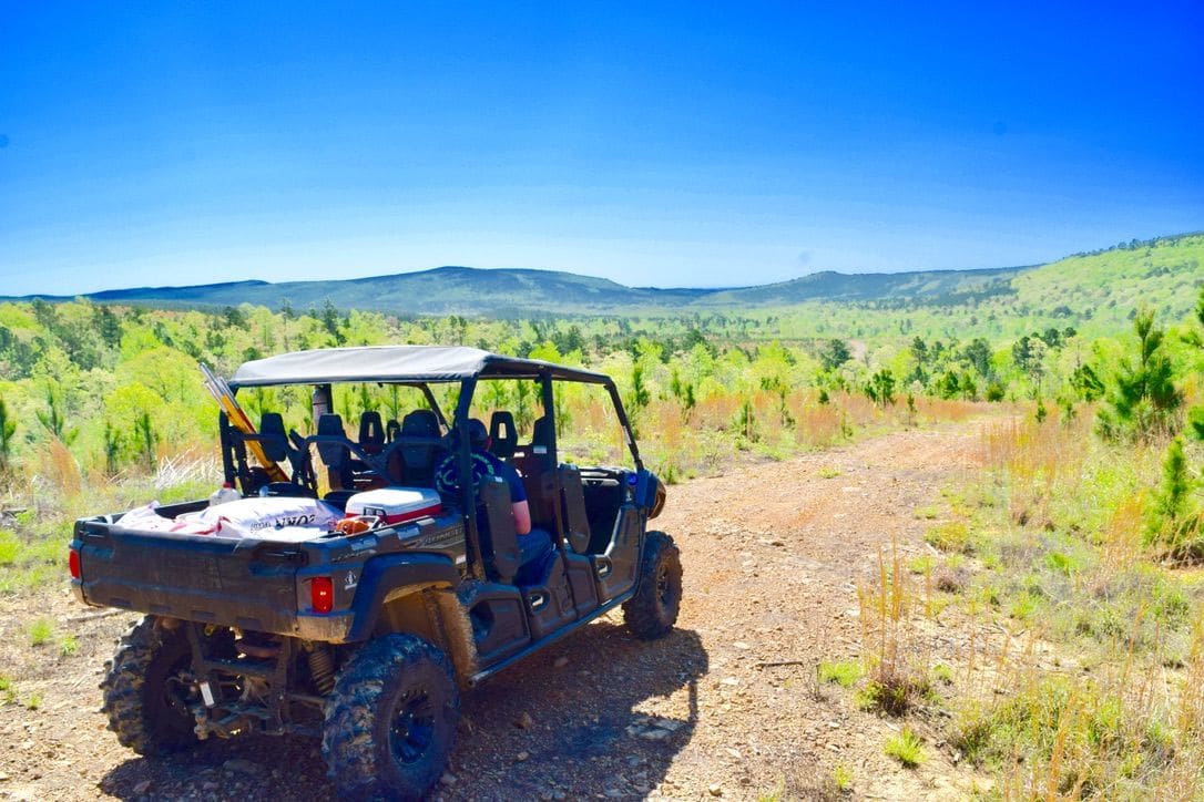A UTV on a dirt road through green hills, with blue sky and mountains