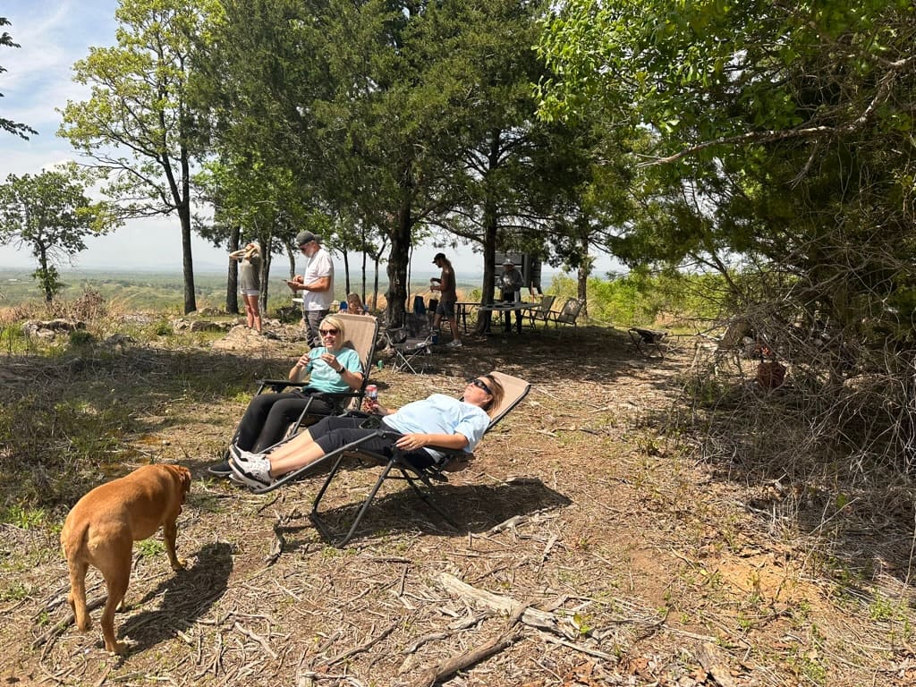 Family relaxing in lawn loungers in the shade on the Panorama Ranch hilltop, with the valley view behind.