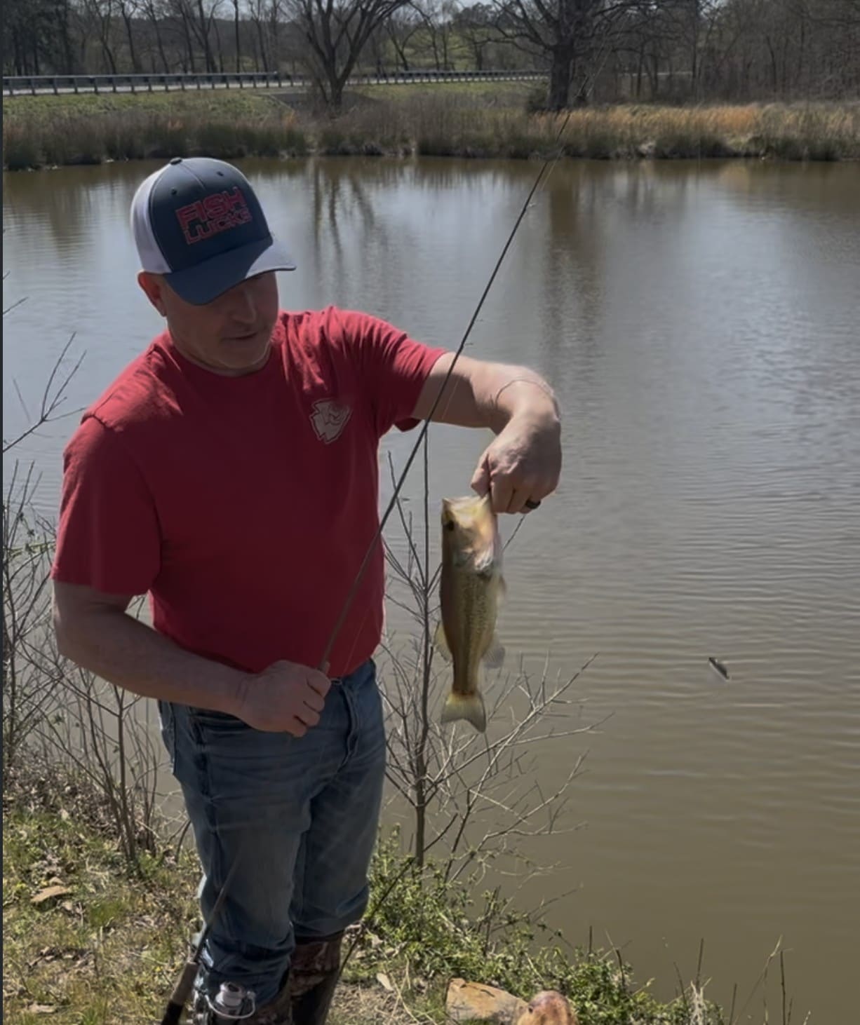 A man holding a largemouth bass on the line beside the stocked fishing pond at Panorama Ranch